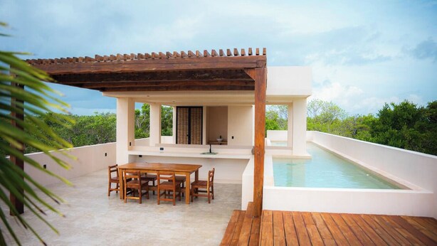 Um pátio moderno ao ar livre com mesa e cadeiras de madeira, piscina e pérgola.