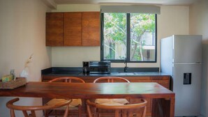 Uma cozinha compacta com armários de madeira, uma mesa de jantar com cadeiras, uma geladeira e uma janela com vista para árvores.