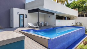 Ein moderner Poolbereich mit einem rechteckigen Pool, Liegestühlen und einer überdachten Sitzgelegenheit.