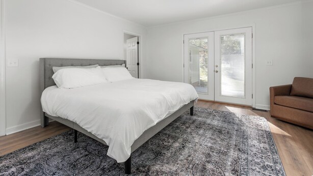 Ein Schlafzimmer mit einem Bett, einem gemusterten Teppich, einem braunen Sofa und einer Tür, die auf einen Balkon führt.