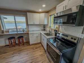 A compact kitchen with white cabinets, a black stove, and a window overlooking a body of water.