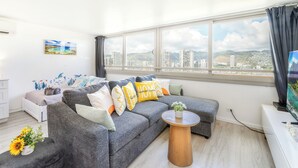 A modern living room with a grey sofa, a round wooden coffee table, and a city view through large windows. - Great View &Waikiki Famliy Retreat (Honolulu)