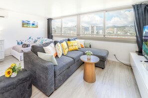 Ein modernes Wohnzimmer mit einem grauen Sofa, einem runden Couchtisch und Blick auf die Stadt durch große Fenster.