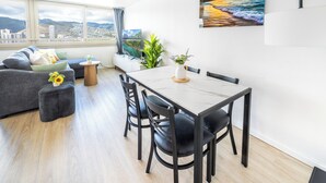 A modern living room with a sofa, dining table, chairs, and a view of a cityscape through large windows. - Great View &Waikiki Famliy Retreat (Honolulu)