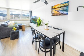 Ein modernes Wohnzimmer mit einer Couch, einem Esstisch, Stühlen und Blick auf eine Stadtkulisse durch große Fenster.