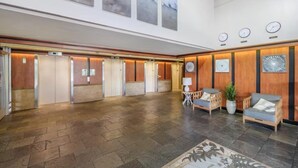 A spacious lobby with a herringbone floor pattern, wooden paneling, and a reception desk with a plant and a lamp. - Great View &Waikiki Famliy Retreat (Honolulu)