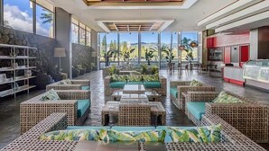 A spacious lobby with wicker furniture, a large window offering a view of palm trees, and a modern ceiling design. - Great View &Waikiki Famliy Retreat (Honolulu)