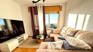 A living room with a flat-screen TV, a sofa, a coffee table, and a window with curtains. - Cc Rooms Porto (Pedrouços)