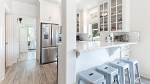 Una cocina moderna con armarios blancos, un refrigerador de acero inoxidable y una encimera con taburetes.