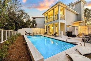 A two-story house with a swimming pool, outdoor seating, and a fenced yard.