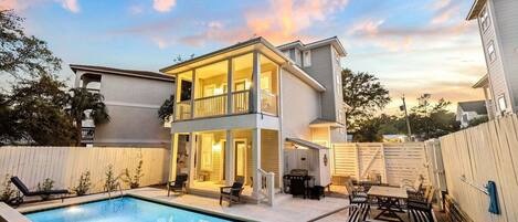 A two-story house with a pool, outdoor seating, and a fenced backyard.