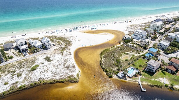 Vista aérea de una zona costera con playa, un río o una desembocadura, y edificios residenciales.