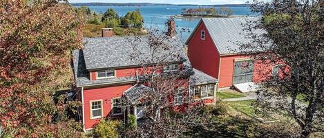 A red house with a large barn-like structure, a sloped roof, and a view of a lake.