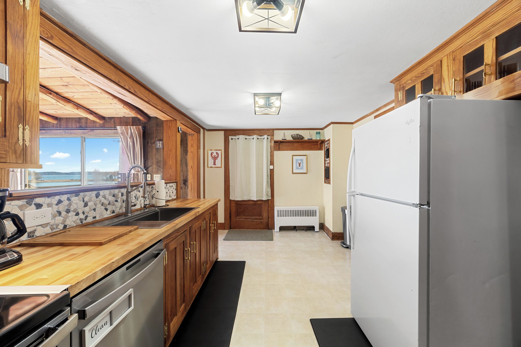 A kitchen with wooden cabinets, a stainless steel refrigerator, a dishwasher, and a window overlooking a scenic view.