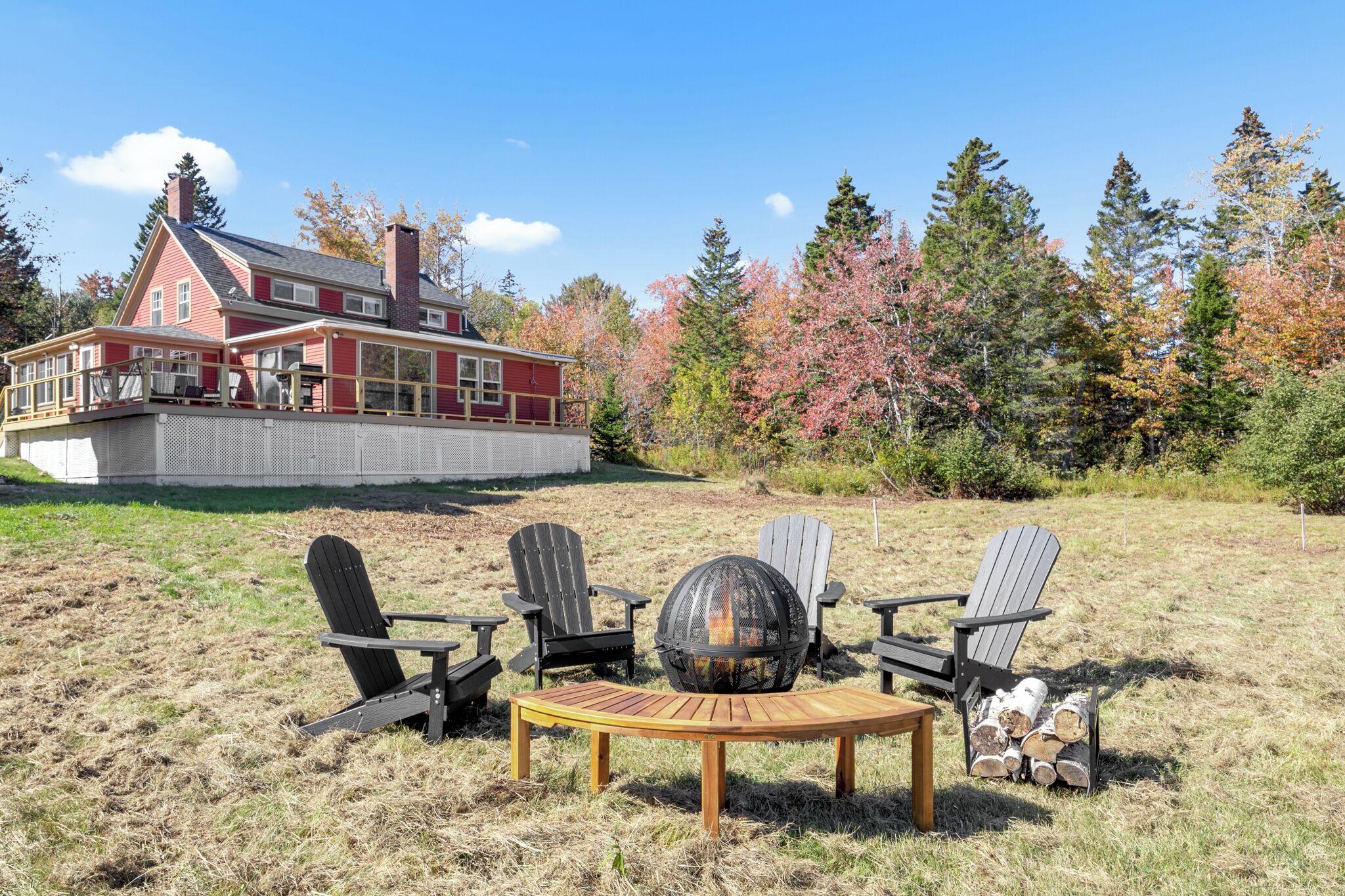 Une maison rouge avec une terrasse, entourée d’arbres aux feuilles d’automne.