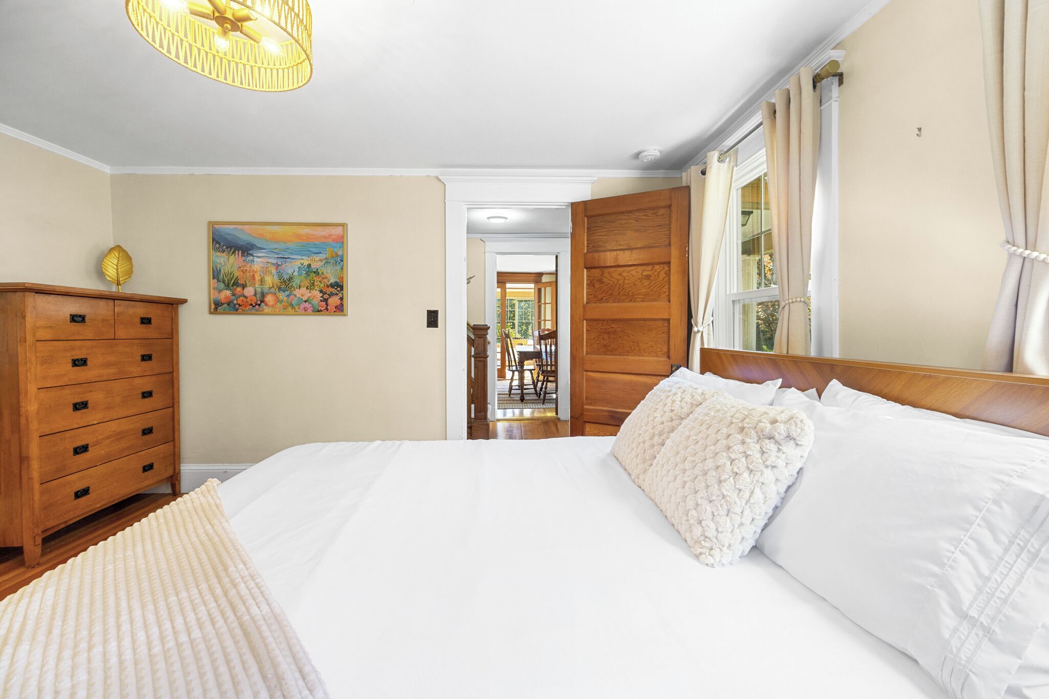 A bedroom with a large bed, wooden dresser, and a painting on the wall.