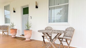 A wooden deck with a round table and four chairs, two potted plants, and a door with a green frame.