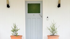 A front door with a green mat, two potted plants, and a wooden porch.