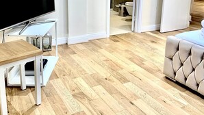 Een moderne woonkamer met een flatscreen televisie op een witte standaard, een beige bank en een houten salontafel.