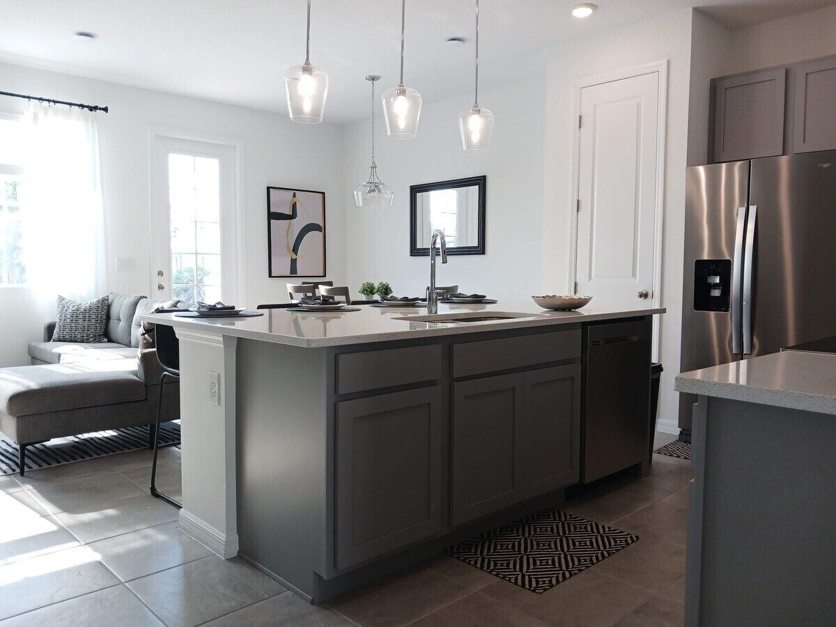 A modern kitchen with a central island, stainless steel appliances, pendant lighting, and a view to the living area.