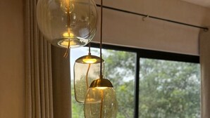 Quarto moderno com uma janela grande, luminária pendente, mesa redonda com um vaso e uma cadeira.
