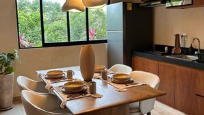 Uma cozinha moderna com uma mesa de jantar de madeira posta para quatro pessoas, uma janela grande com vista para o verde e um micro-ondas embutido sobre a bancada.