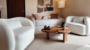 Uma sala de estar moderna com um sofá branco, uma mesa de centro de madeira e uma tapeçaria na parede.