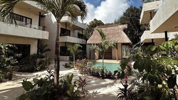 Pátio moderno de hotel com piscina, palmeiras e estrutura com telhado de palha.