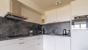 A modern kitchen with white cabinets, a black countertop, and stainless steel appliances. - 4-person Apartment With Island-sea View (De Koog)