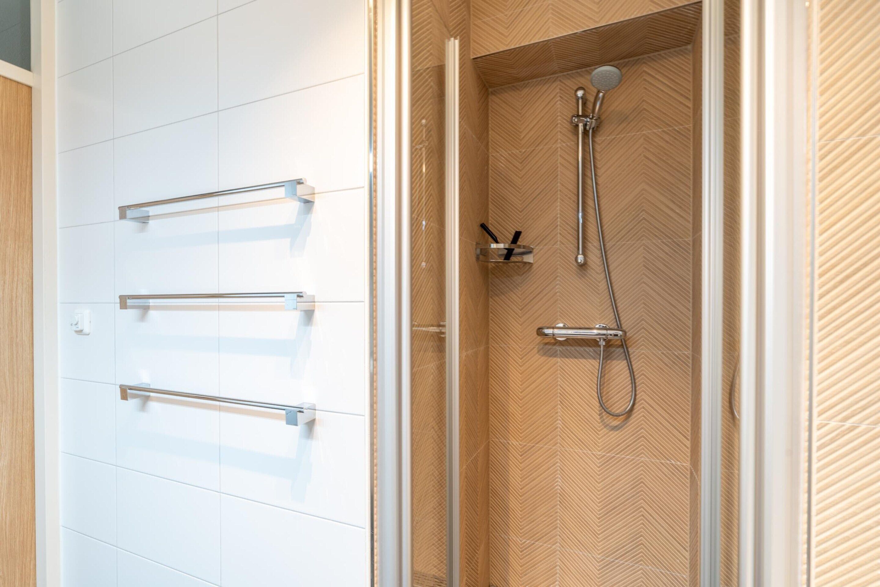 Een douche met een wand van hout in visgraatmotief, een glazen deur en een metalen handdoekhouder.