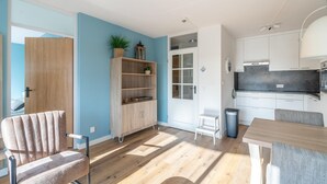 Une cuisine moderne avec des armoires blanches, un comptoir noir et un four encastré. On y trouve une chaise en bois et une petite table avec un coussin gris.