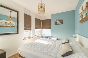 A bedroom with a large bed, two windows with blinds, a ceiling light fixture, and artwork on the walls. - 4-person Apartment With Island View (De Koog)