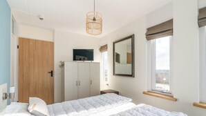 Une chambre à coucher comprenant un lit, une armoire, une télévision, un miroir et une fenêtre donnant sur un beau paysage.