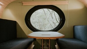 Un intérieur petit et chaleureux, avec une fenêtre ronde, deux coins salon agrémentés de coussins et une petite table.