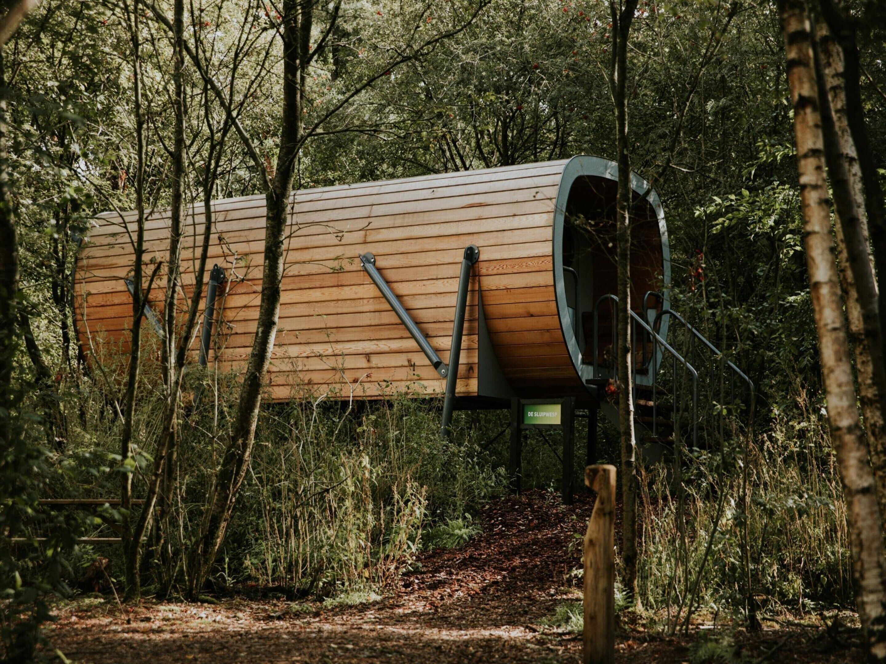 A cylindrical wooden cabin with a curved entrance, surrounded by dense forest.