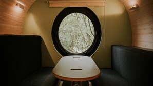 Une pièce circulaire et accueillante, dotée d’une fenêtre ronde, d’une petite table et de deux coins salon agrémentés de coussins.