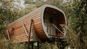 Une cabane en bois avec un toit incurvé, un petit porche et une enseigne sur laquelle on peut lire « DE SLUIPWESE ».