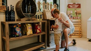 A man and a child in a room with wooden shelves displaying snacks and bottles. - Charming 5-person Bee Lodge in the Woods (Balkbrug)
