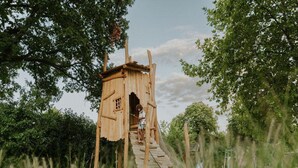 A wooden playhouse with a ladder leading up to it, surrounded by trees and grass. - Charming 5-person Bee Lodge in the Woods (Balkbrug)
