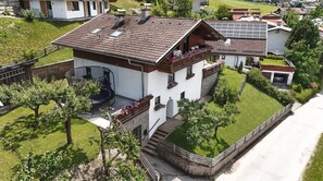 A two-story house with a sloped roof, a balcony with potted plants, and a small outdoor seating area. - Alpenchalet Berggold - Holiday Home With Panoramic Views (Tulfes)