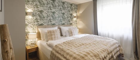 A hotel room with a bed, a nightstand, a lamp, a wall with a nature-themed wallpaper, and a window with curtains.