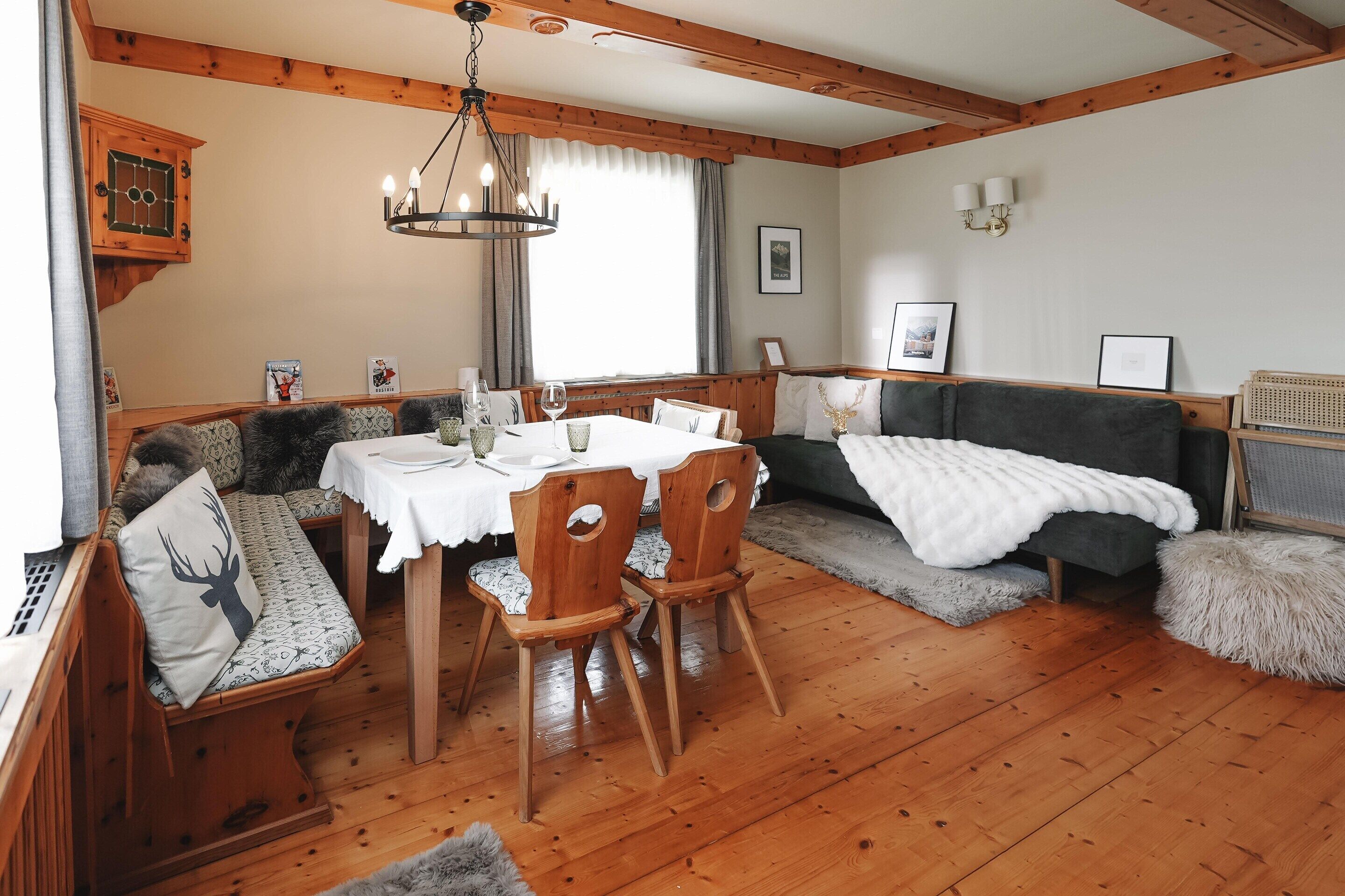 Et hyggeligt rum med et træspisebord, stole, en bænk med hynder, en sofa og en seng.
