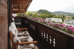A balcony with a wooden chair, a view of a residential area, and a flower bed. - Alpenchalet Berggold - Holiday Home With Panoramic Views (Tulfes)