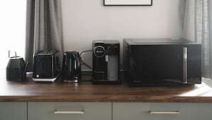 Uma cozinha compacta com cafeteira, torradeira e micro-ondas em bancada de madeira.