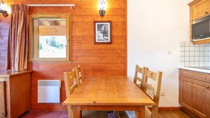 Un interno in legno con un tavolo da pranzo, sedie, una finestra con tende, un quadro appeso al muro e un angolo cottura con un forno a microonde.