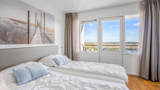 Ein Schlafzimmer mit zwei Betten, einem großen Fenster mit Vorhängen und Blick auf die Landschaft.
