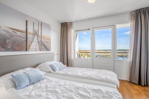 Ein Schlafzimmer mit zwei Betten, einem großen Fenster mit Vorhängen und Blick auf die Landschaft.