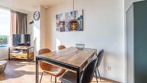 Ein modernes Wohnzimmer mit einem Holzesstisch, Ledersesseln, einem Flachbildfernseher und einem großen Fenster mit Vorhängen.