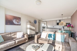 A modern living room with a sofa, coffee table, and a painting of a dandelion on the wall. - 4-person Apartment With Island View (De Koog)