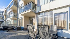 A modern outdoor patio with a table and chairs, a sofa, and a glass balustrade. - 4-person Apartment With Island View (De Koog)